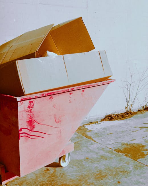 A pile of discarded household items and construction debris arranged outdoors on a paved surface, including leaning wooden pallet-like structures, torn and damaged furniture with peeling paint, and a