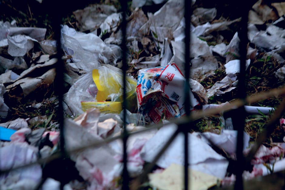 A large pile of discarded metal scrap consisting of rusty steel pipes, bent and broken metal beams, and twisted metal rods, some partially covered in peeling blue or brown paint. The scrap appears to 