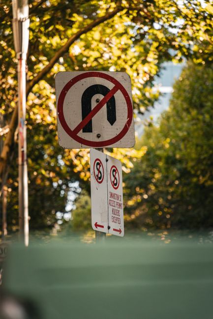 A rectangular illuminated sign mounted on a beige brick wall features a red border and text indicating 'NO PARKING IN ALLEY' in purple capital letters. To the left of the text, there is a circular red